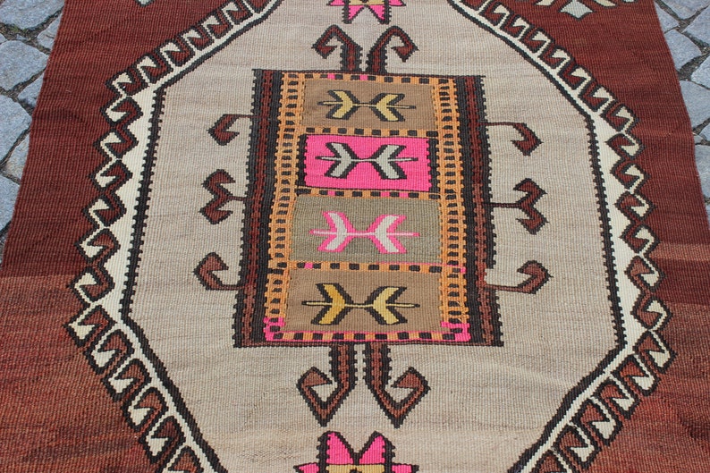 May include: A vintage Turkish rug with a geometric pattern in shades of brown, beige, pink, and orange. The rug has a central medallion with a repeating arrow design.