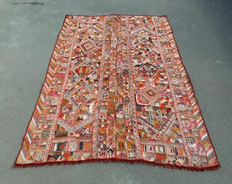 May include: A rectangular textile wall hanging or rug featuring a dense, multi-colored patchwork of embroidered geometric shapes, diamond patterns, and intricate motifs in shades of red, orange, yellow, blue, and white with a fringed border.