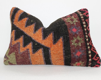 May include: A colorful, handwoven pillow cover with a geometric pattern in shades of orange, black, purple, green, and pink. The pillow cover has a fringed edge.