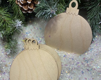 May include: A set of unfinished light brown wooden ornaments in a circular bauble shape with a small loop at the top for hanging. The smooth, flat wooden surfaces are blank and circular, featuring a distinct grain pattern throughout the wood.