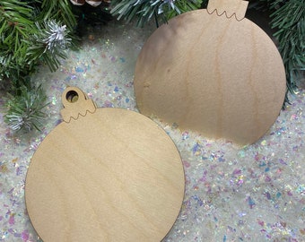 May include: Two unfinished wooden ornaments shaped like Christmas tree ornaments. The ornaments are on a white background with iridescent glitter.