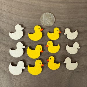 May include: A set of 12 wooden duck ornaments, half painted yellow with orange beaks and half left unpainted. The ducks are approximately the size of a US quarter.
