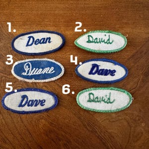 May include: A collection of six vintage name patches. The patches are oval-shaped, with embroidered names in various colors. Names include "Dean", "David", "Duane", and "Dave". The patches have a white background with colored borders.