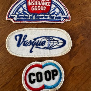 May include: Three vintage embroidered patches. The top patch reads "FARMERS INSURANCE GROUP" in red and white on a blue and white shield. The middle patch says "Vasque" with a globe design. The bottom patch says "COOP" in black, red, and blue.