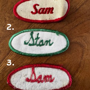 May include: Three vintage name patches. The first patch is oval-shaped with a red border and the name "Sam" embroidered in red. The second patch has a green border and the name "Stan" embroidered in green. The third patch is oval-shaped with a red border and the name "Sam" embroidered in red.