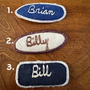 以下が含まれることがあります： 刺繍された名前が書かれた3つのヴィンテージネームパッチ。最初のパッチは青色で、白い文字で「Brian」と書かれています。2番目はオフホワイトで、茶色の文字で「Billy」と書かれています。3番目は濃い青色で、白い文字で「Bill」と書かれています。