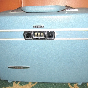 May include: A light blue hard-shell travel case with a textured finish, a top handle, and a central combination lock. The case features a white horizontal trim, silver-tone metal hardware, and the brand name Sears printed on the front latch.