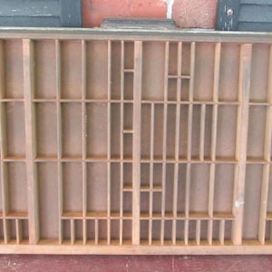 May include: A vintage wooden printer's tray with numerous small compartments of varying sizes. The tray is rectangular and made of light-colored wood, likely pine or a similar material. It is designed for organizing small items or displaying collectibles.