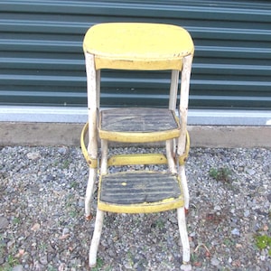May include: Vintage yellow and white step stool with three steps and a seat. The steps and seat are yellow, and the frame is white. The step stool is made of metal and has a folding design. The stool is approximately 30 inches tall.