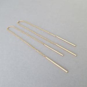 Op de afbeelding: Een paar gouden kettingoorbellen met vier hangende gouden staven.