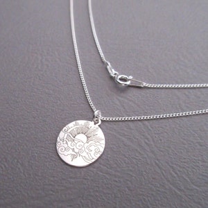 May include: A silver necklace with a round pendant featuring an engraved design of a sun rising above clouds.