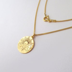 Può includere: Una collana d'oro con un ciondolo rotondo che presenta un design inciso di un sole che sorge sopra le nuvole.