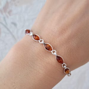 May include: A silver bracelet with oval amber stones. The amber stones are a warm, translucent brown colour and are linked with silver connectors. The bracelet is displayed on a wrist.