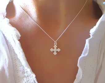 May include: A silver necklace with a small, ornate cross pendant featuring five clear gemstones. The cross is a simple, classic design.