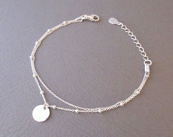 May include: A silver chain bracelet with a small round charm. The bracelet has two chains with small beads on one chain.