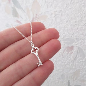 Könnte beinhalten: Eine silberne Schlüsselkette mit einer zarten Kette. Der Schlüsselanhänger hat ein verziertes Design mit einer abgerundeten Oberseite und einem langen, dünnen Stiel.