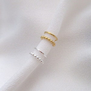 Könnte beinhalten: Zwei Ohrringe in Form von Manschetten, einer in Gold und einer in Silber. Die Ohrringe sind aus Metall und haben ein schlichtes Design.