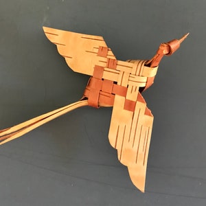 May include: A woven bird sculpture made of brown and tan strips of material. The bird has a long tail and outstretched wings.