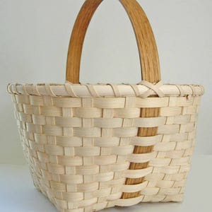 May include: A woven basket with a natural wood handle. The basket is made of light brown and white woven strips.