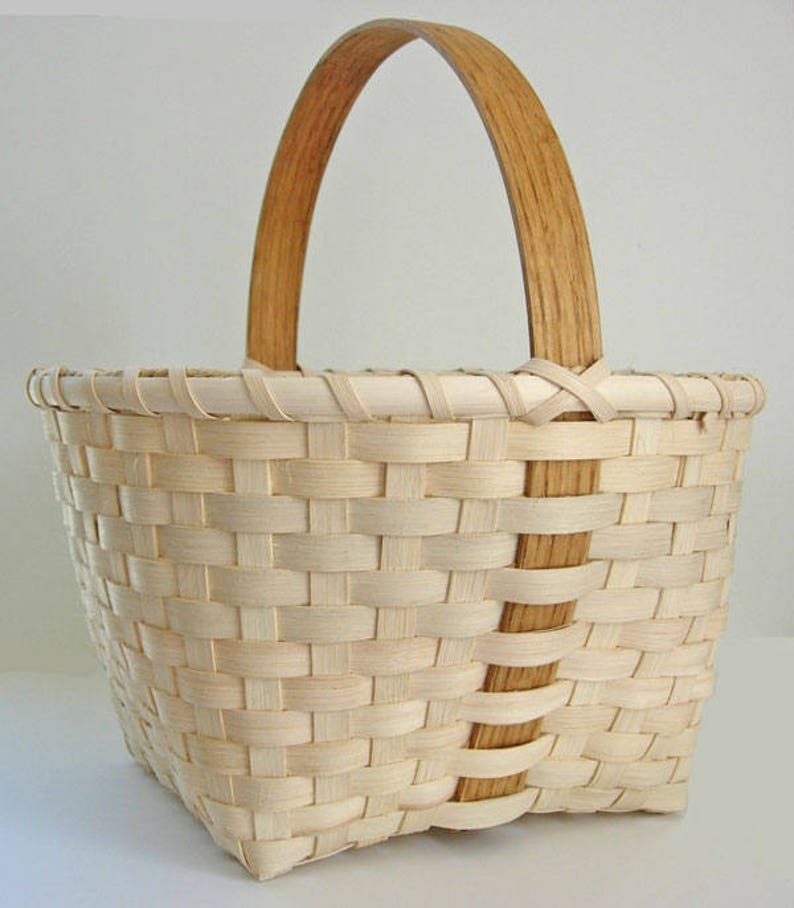 May include: A woven basket with a natural wood handle. The basket is made of light brown and white woven strips.