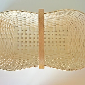 May include: A woven basket with a natural wood handle. The basket is made of light brown, woven material and has a rectangular shape.