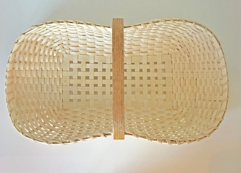 May include: A woven basket with a natural wood handle. The basket is made of light brown, woven material and has a rectangular shape.