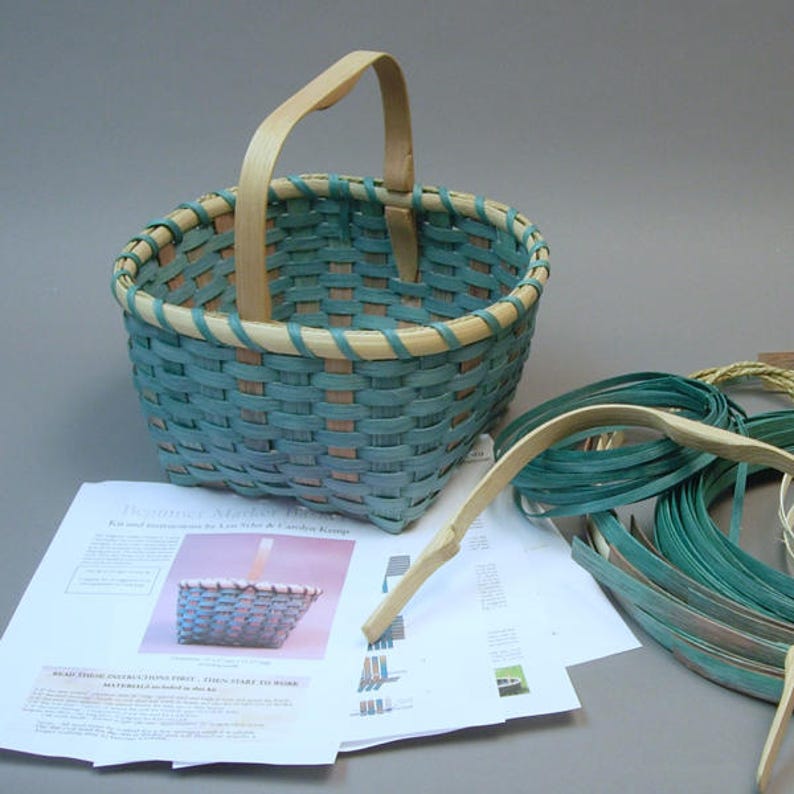 May include: A teal and natural woven basket with a wooden handle. The basket is partially assembled with additional weaving materials and instructions visible in the background.