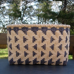 May include: A woven basket with a geometric pattern of beige and dark gray. The basket is made of natural materials and has a rounded shape.