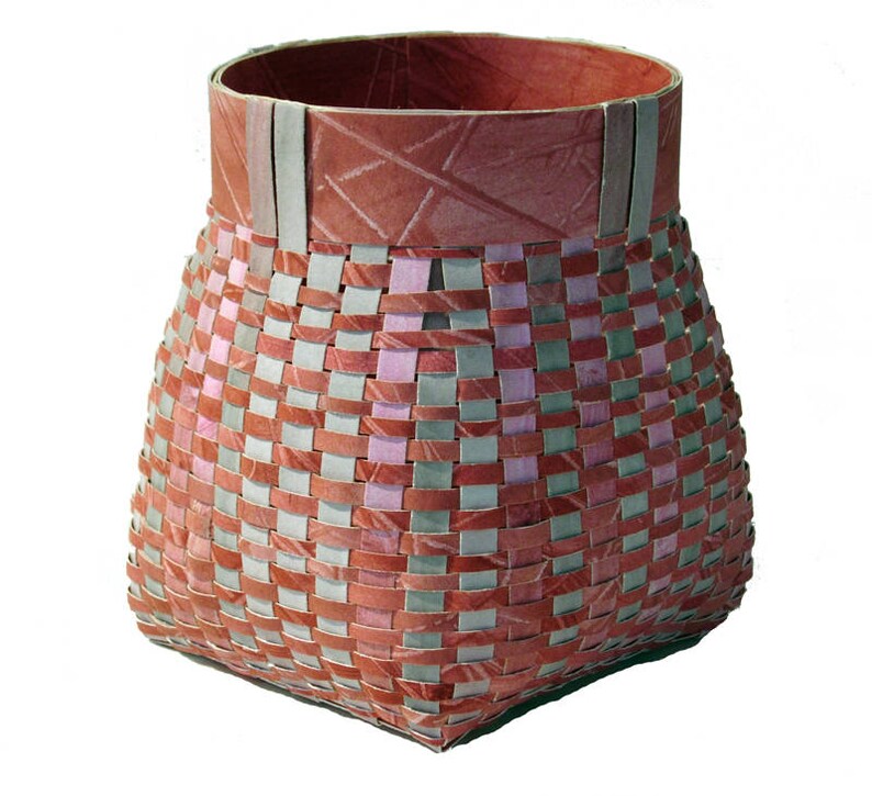 May include: A woven basket with a square base and a rounded top. The basket is made of strips of paper in shades of pink, red, and grey. The top rim of the basket is a solid red.