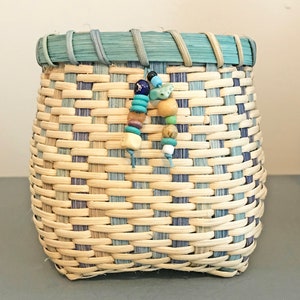 May include: A small woven basket with a blue and white striped pattern. The basket has a blue rim and is decorated with colourful beads.