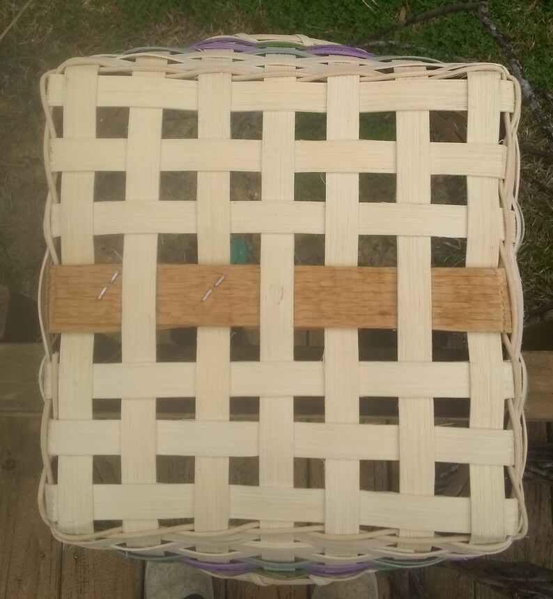 Op de afbeelding: Een geweven mand met een lichtbruine houten handvat. De mand is gemaakt van natuurlijke materialen en heeft een lichtbeige kleur. De mand is geweven in een rasterpatroon.