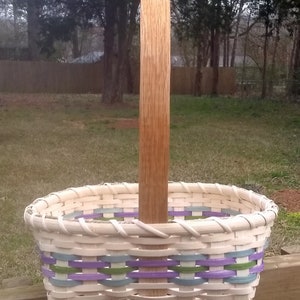 May include: A white wicker basket with a wooden handle. The basket has purple, green, and blue stripes around the rim.