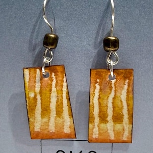 May include: A pair of dangle earrings featuring rectangular pendants with a watercolor-style gradient of orange, yellow, and white vertical stripes. Each pendant hangs from a silver-toned hook with a small, dark metallic bead above the jump ring.