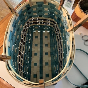 May include: A woven basket with a blue and white pattern is being assembled. The basket is held together with wooden clothes pegs.