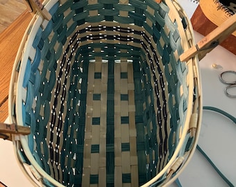 May include: A woven basket with a blue and white pattern is being assembled. The basket is held together with wooden clothespins.