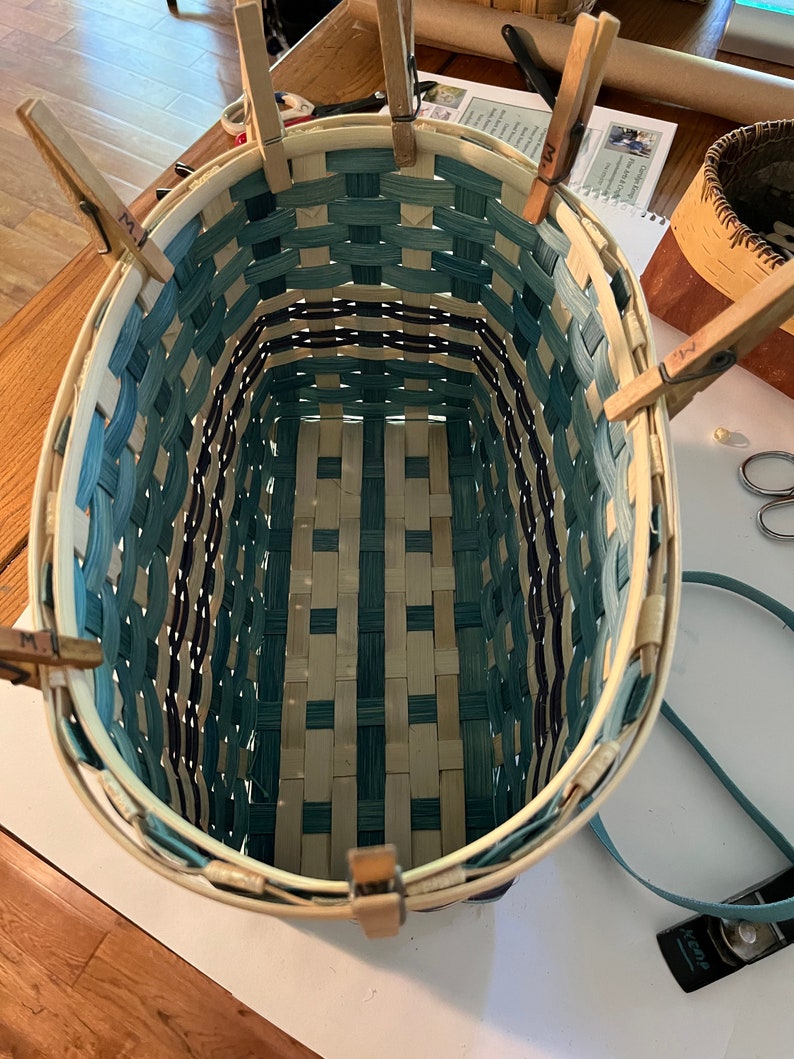 May include: A woven basket with a blue and white pattern is being assembled. The basket is held together with wooden clothes pegs.