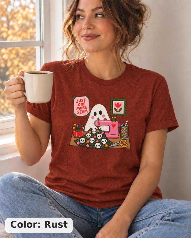 Woman holding a mug, wearing a Rust (deep red-brown) t-shirt with the "Just One More Seam" folk-art ghost sewing print. Color: Rust.