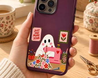 May include: A dark purple smartphone case featuring a graphic of a white ghost sewing with a pink machine. The design includes a floral fabric piece, a red pincushion, a green drink, and a sign that reads JUST ONE MORE SEAM with a small flower picture.