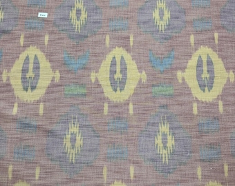 Puede incluir: Primer plano de una tela marrón con un patrón repetido de diseños ikat amarillos, azules y morados. La tela tiene una textura sutil y una apariencia ligeramente descolorida.