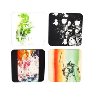 May include: Set of four square coasters featuring an astronaut in different colour schemes. The coasters have a white, black, rainbow, and green background with the astronaut in a different colour on each.