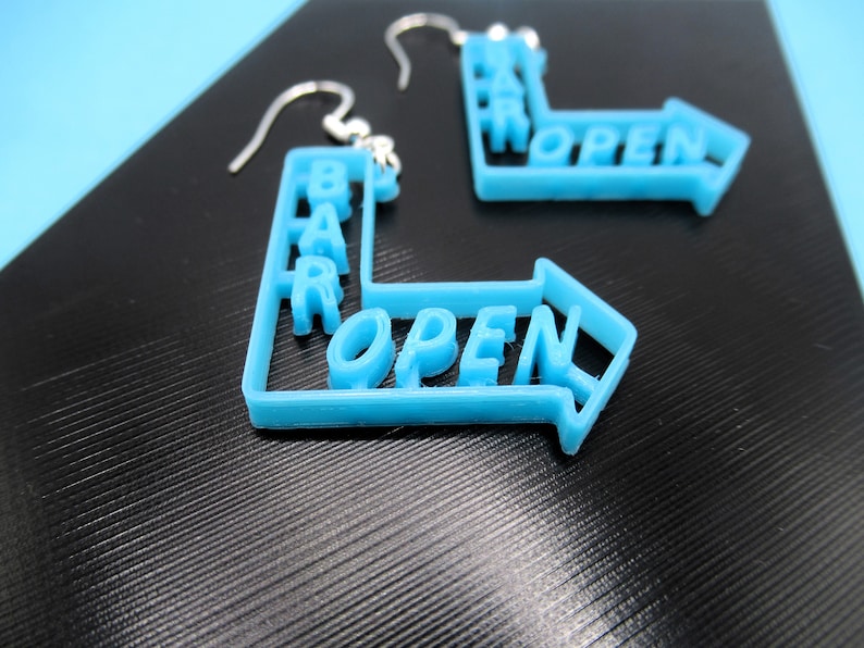 May include: A pair of blue earrings shaped like a directional arrow with the words "BAR OPEN" written on them.