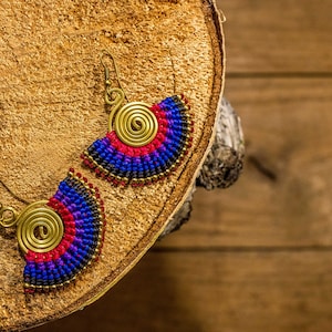 May include: A pair of handmade earrings with a spiral design and colorful beads. The earrings are blue, red, and black.