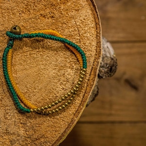 May include: A green and yellow braided bracelet with gold beads and a small bell charm.