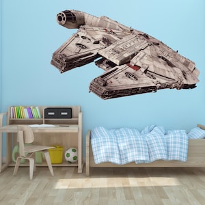 May include: A white and gray spaceship wall decal with a red stripe,  mounted on a light blue wall in a child's bedroom. The decal is above a wooden bed with a blue and white plaid comforter and a wooden desk with a chair and books.