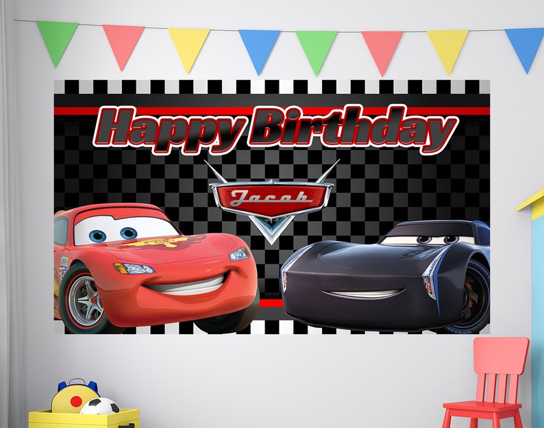 May include: A black and white checkered background with the words "Happy Birthday" in red. The name "Jacob" is in red on a red and silver car logo. A red car with a smiling face and a black car with a smiling face are on either side of the logo.