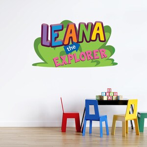 May include: A colorful wall decal with the text "Leana the Explorer" in a green, yellow, blue, pink, and purple font. The decal is on a white wall with a table and four colorful chairs in front of it.