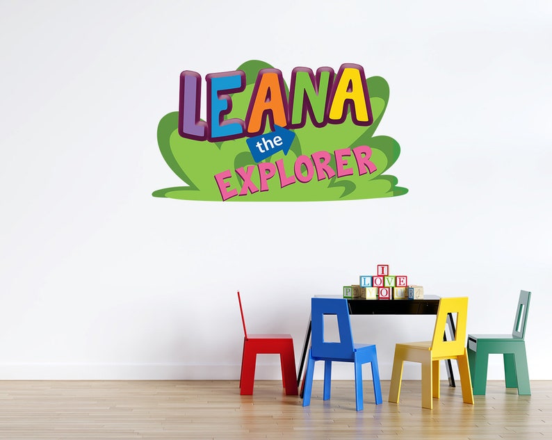 May include: A colorful wall decal with the text "Leana the Explorer" in a green, yellow, blue, pink, and purple font. The decal is on a white wall with a table and four colorful chairs in front of it.