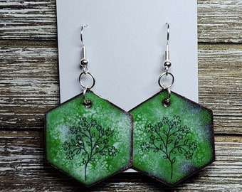 May include: A pair of green hexagonal earrings with a silver hook and a delicate floral design. The earrings are on a white card with the text "Ashley Rose Earrings".