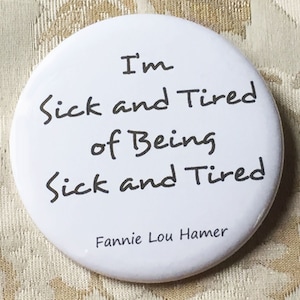 May include: White button with black text that reads "I'm sick and tired of being sick and tired" and "Fannie Lou Hamer" at the bottom.