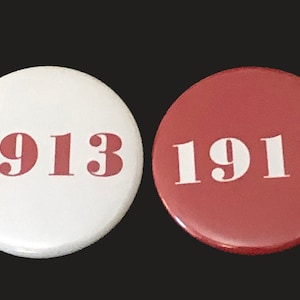 May include: Two round buttons with the year 1913 printed on them. One button is white with red lettering and the other is red with white lettering.